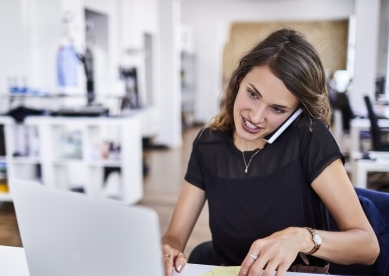 Woman on cell phone and working on laptop in office